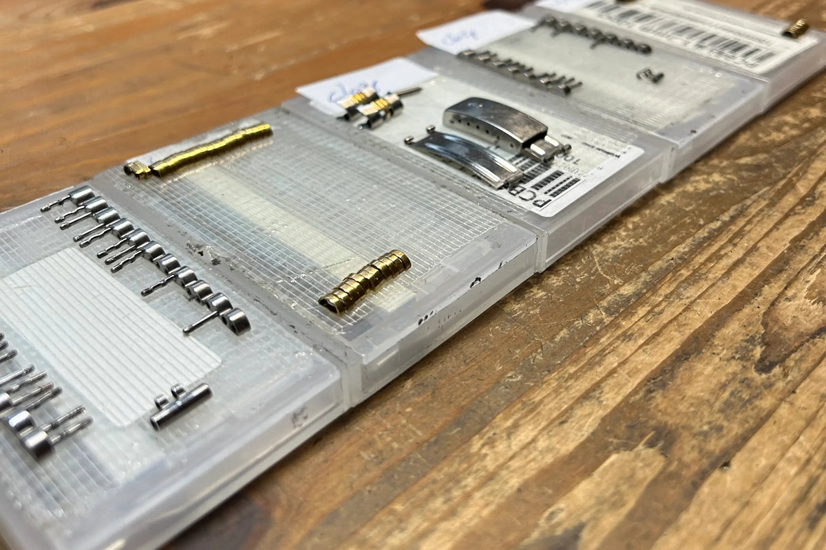 Metal links, pins, and individual watch bracelet components carefully arranged on a workbench for restoration.